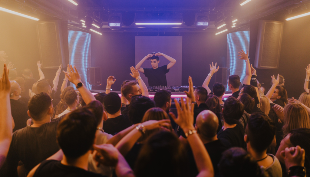 Live DJ performance on stage with an energetic crowd and dynamic lighting, depicting a vibrant nightlife scene.
